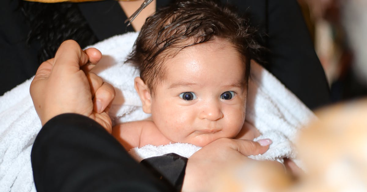 A baby wrapped in a towel, gently held by a person, symbolizing warmth and care during a naming ceremony.