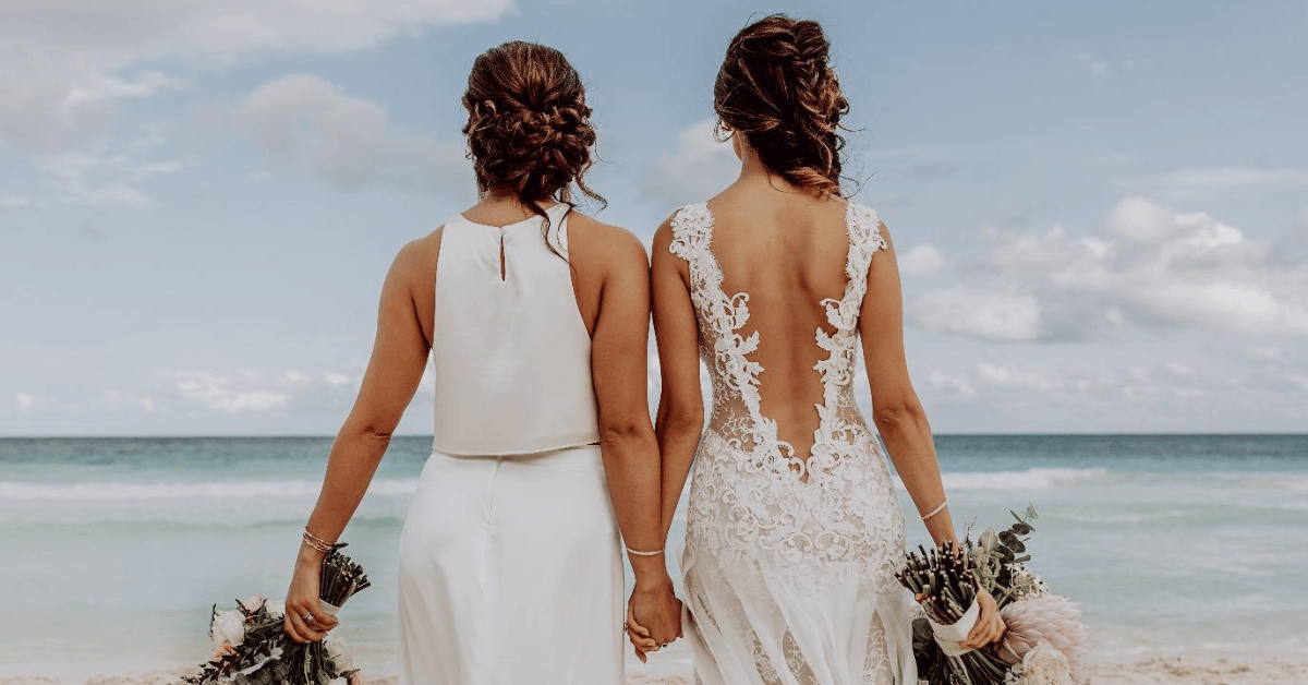 Two brides holding hands on the beach, celebrating their love with a marriage celebrant officiating their wedding.